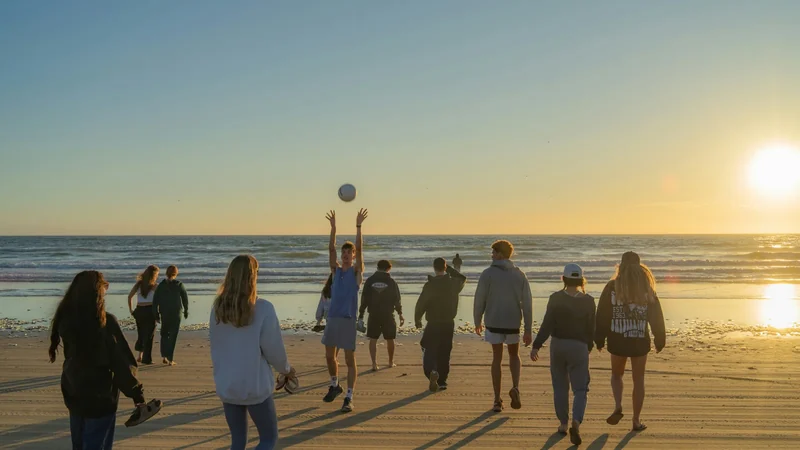 A group on the beach at sunset, with a boy tossing a ball into the air